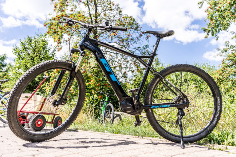 Sort cykel står på fortovet ved siden af træer.